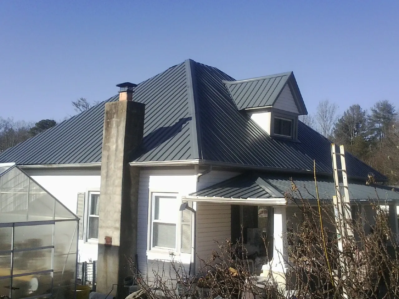 Dark blue standing seam metal roof on a white farmhouse with dormer — Slate & Tile Roof Repair by Roofing Brothers in Crozier