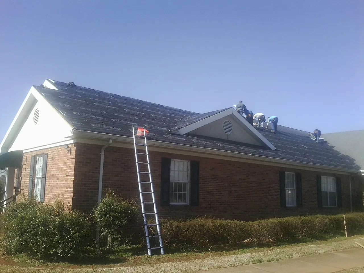 Crew tearing shingles off a brick ranch roof with a ladder set — Emergency Roof Repair work by our crew in Crozier