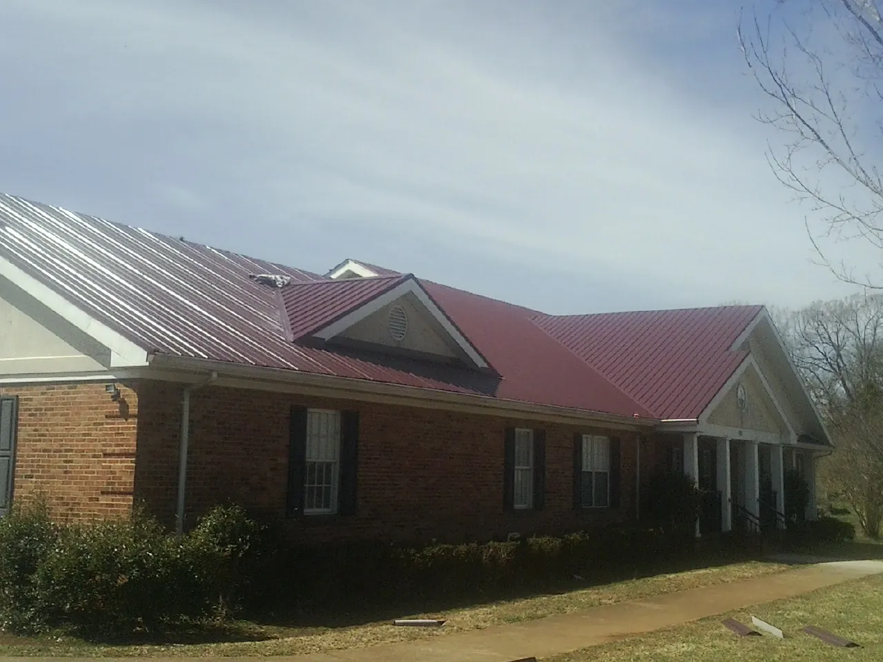 Red metal roof with gabled entries on a long brick building, from a Hail Damage Roof Repair job in Crozier
