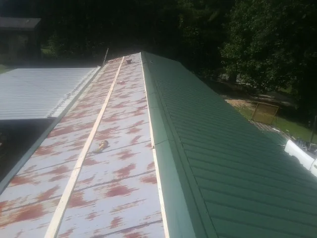 Old rusted panels beside newly installed green metal roofing — Wind Damage Roof Repair by Roofing Brothers in Crozier