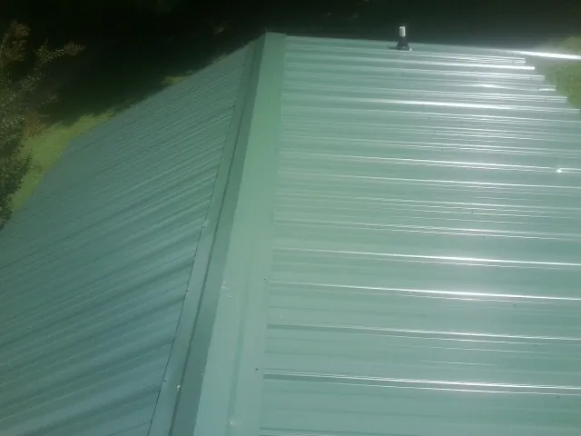New green metal panels meeting at the ridge of a roof — Flat Roof Repair work by our crew in Crozier