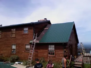 Green metal roof going on a two story log home with ladders set in Crozier