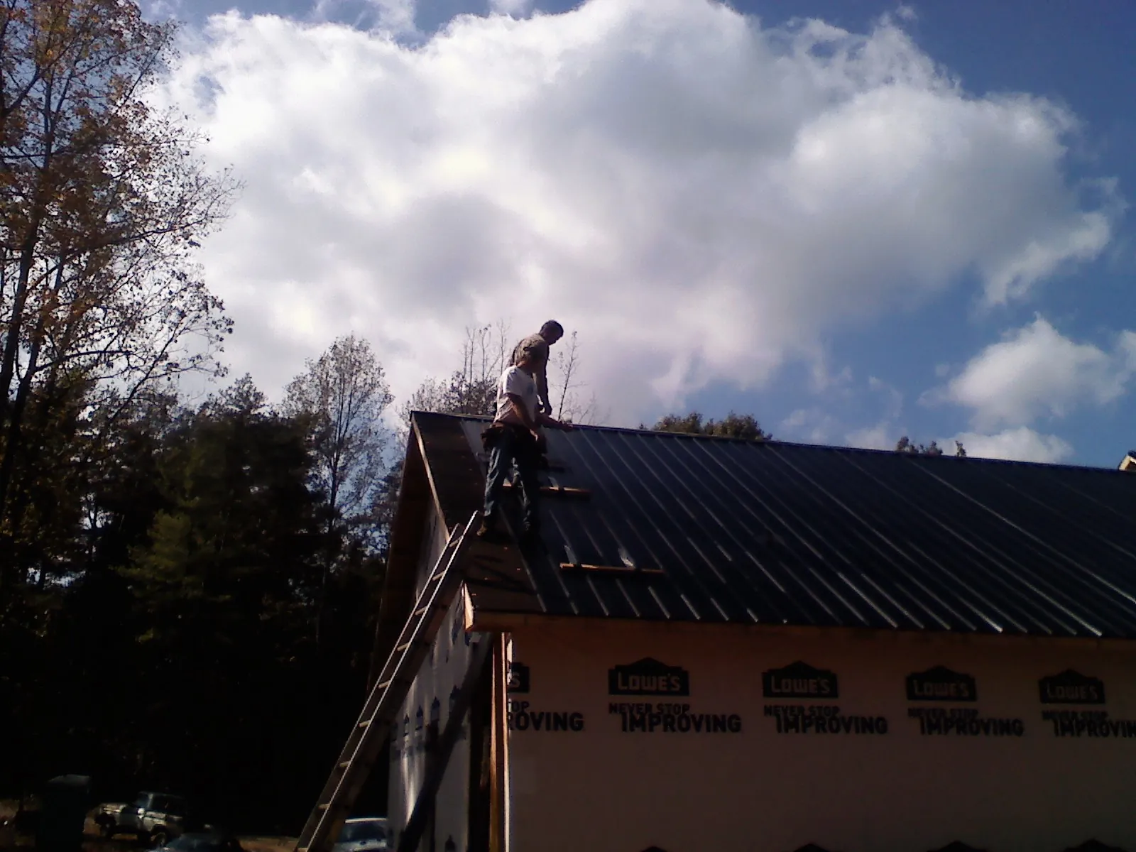 Roofer fastening dark metal panels high against a cloudy sky, from a Roof Inspection job in Crozier