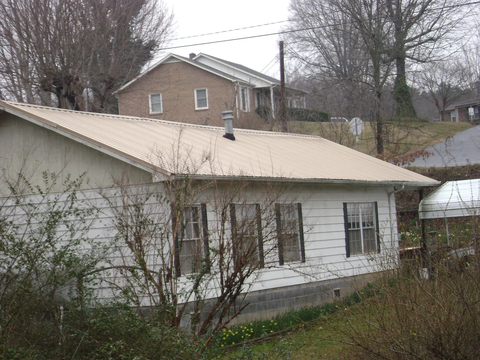Tan metal roof on a white sided house set into a hillside — Commercial Roofing by Roofing Brothers in Crozier